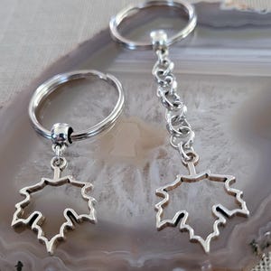 May include: Two silver keychains with a maple leaf charm. The keychains are attached to silver key rings.