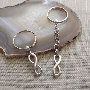 May include: Two silver infinity symbol keychains. One keychain has a silver chain and the other has a silver ring.