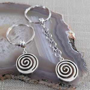 May include: Two silver keychains with a spiral design. The keychains are on a gray and white agate background.