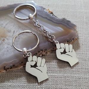 May include: Two silver keychains with a raised fist design. The keychains are attached to silver key rings.
