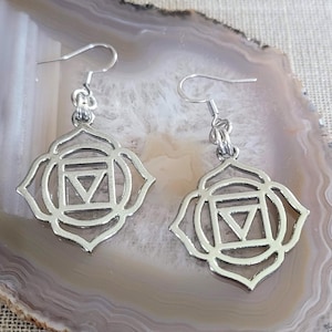 May include: A pair of silver-colored earrings. Each earring features a stylized lotus flower design with a central geometric shape. The earrings have a hook closure.