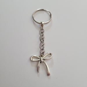 May include: A silver key chain with a bow charm. The chain is attached to a silver ring.