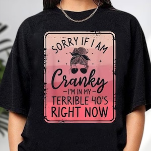May include: Black crew neck t-shirt with a distressed pink and white graphic. The graphic reads "Sorry if I am Cranky - I'm in my terrible 40's right now" with a woman's face wearing sunglasses and a bun.