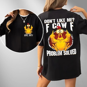 May include: Black t-shirt featuring a cartoon chicken giving the middle finger. The front of the shirt has a smaller graphic with "EST. 1977". The back of the shirt has the text "DON'T LIKE ME? F CAW F PROBLEM SOLVED".