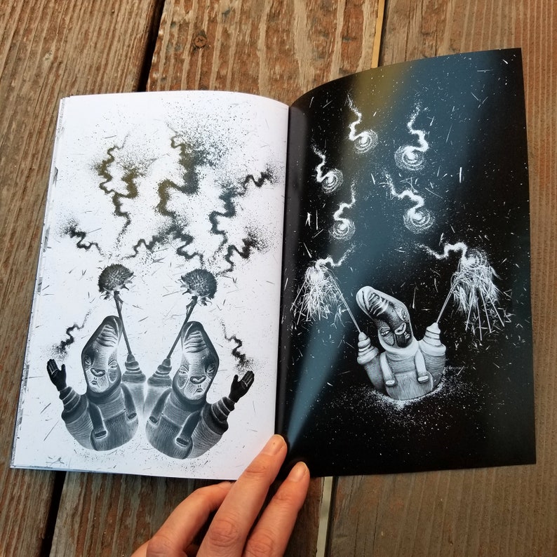 May include: An open book with black and white illustrations. The left page shows two figures with sparklers, while the right page shows a single figure with sparklers against a dark, starry background.