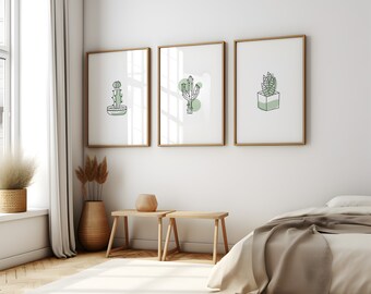 May include: Three framed art prints featuring minimalist cactus illustrations in green and black on a white background. The frames have a gold finish. The artwork is displayed in a bright, modern bedroom setting.