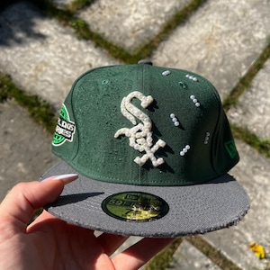 Może przedstawiać: Ciemnozielona czapka z daszkiem w kolorze szarym, z logo Chicago White Sox ozdobionym białymi perłami z przodu. Czapka posiada rozrzucone białe perły z boku, naszywkę World Series oraz naklejkę 59FIFTY na daszku o rozmiarze 58,7 cm.