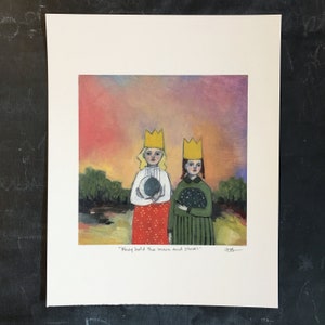 May include: A matted art print featuring two figures wearing yellow crowns against a sunset sky. One figure wears a white top and red skirt holding a moon, the other a green dress holding a star-filled sphere. Text reads: "They held the moon and stars".