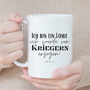Könnte beinhalten: Weiße Keramiktasse mit schwarzem Text, der "Ich bin ein Löwe ich wurde von Kriegern erzogen! - Maurice -" lautet.