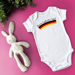 Peut inclure: Combinaison blanche pour bébé avec un motif de drapeau allemand noir et jaune et le texte "Kleister Fanfrosster Jubel!"