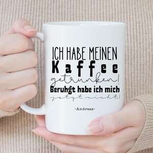 May include: White ceramic coffee mug with black text that reads "ICH HABE MEINEN Kaffee getrunken! Beruhigt habe ich mich jetzt nicht!" and the name "-Andreas-". The mug is held by a person.