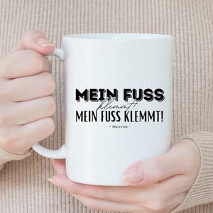 Può includere: Tazza in ceramica bianca con testo nero che recita "Mein Fuss klemmt! Mein Fuss klemmt! - Maurice -"