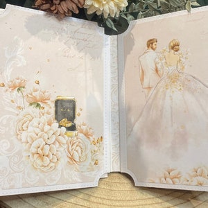 Può includere: Un album di nozze bianco con un design floreale sulla copertina. L'album è aperto per rivelare un'illustrazione ad acquerello di una sposa e uno sposo.