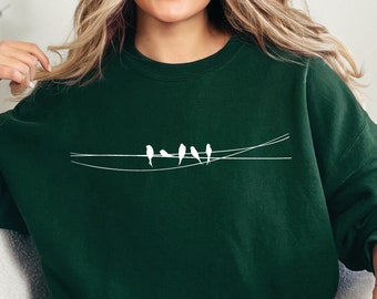 May include: A dark green sweatshirt with a white graphic of five birds on a wire. The sweatshirt has a crew neck and long sleeves.