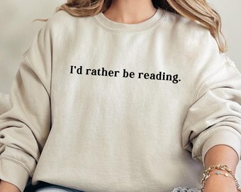 May include: A beige sweatshirt with the text "I'd rather be reading." printed on the front. The model is wearing blue jeans.