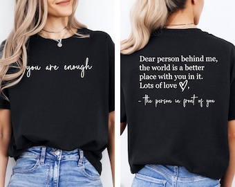 May include: Black t-shirt with white text on the front that reads "you are enough." The back of the shirt has a message: "Dear person behind me, the world is a better place with you in it. Lots of love, - the person in front of you."