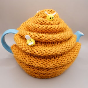 May include: A yellow knitted teapot cosy shaped like a honeycomb with two small yellow and white bee decorations.