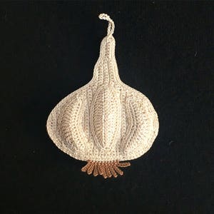 May include: A crocheted garlic bulb with a brown stem. The garlic is white and has a textured surface.