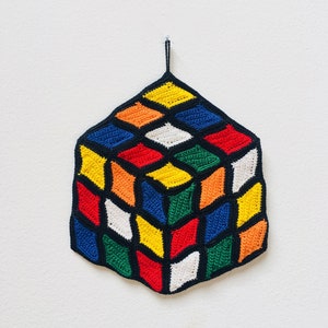 May include: A crocheted cube with a black outline and a variety of colors including red, green, yellow, blue, white, and orange.