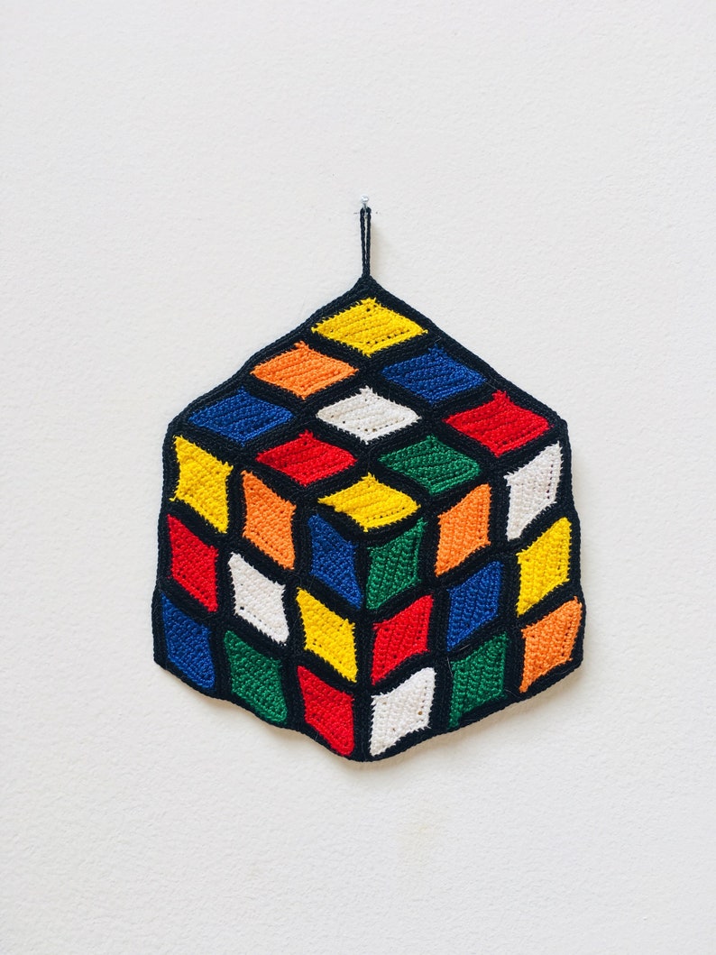 May include: A crocheted cube with a black outline and a variety of colors including red, green, yellow, blue, white, and orange.