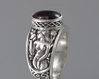 May include: A silver ring with a red gemstone and an intricate design of a woman standing in a garden. The ring is set with a red gemstone and has a detailed design of a woman standing in a garden. The ring is made of silver and has a polished finish.