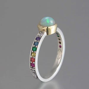 May include: A silver ring with a white opal gemstone set in a gold bezel. The band is decorated with a rainbow of small gemstones.