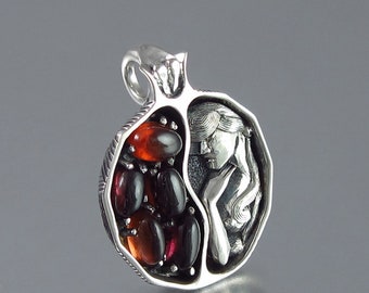 May include: A silver pendant in the shape of a pomegranate, with a detailed carving of a woman's face and hair on one side. The other side is filled with red and black gemstones.