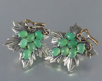 May include: A pair of silver earrings shaped like grapevines with green gemstones. The earrings feature a detailed design of leaves and vines with a cluster of green gemstones representing grapes.