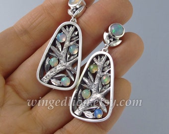May include: Silver earrings with a tree design and opal stones. The earrings are shaped like a teardrop and have a delicate, intricate design.