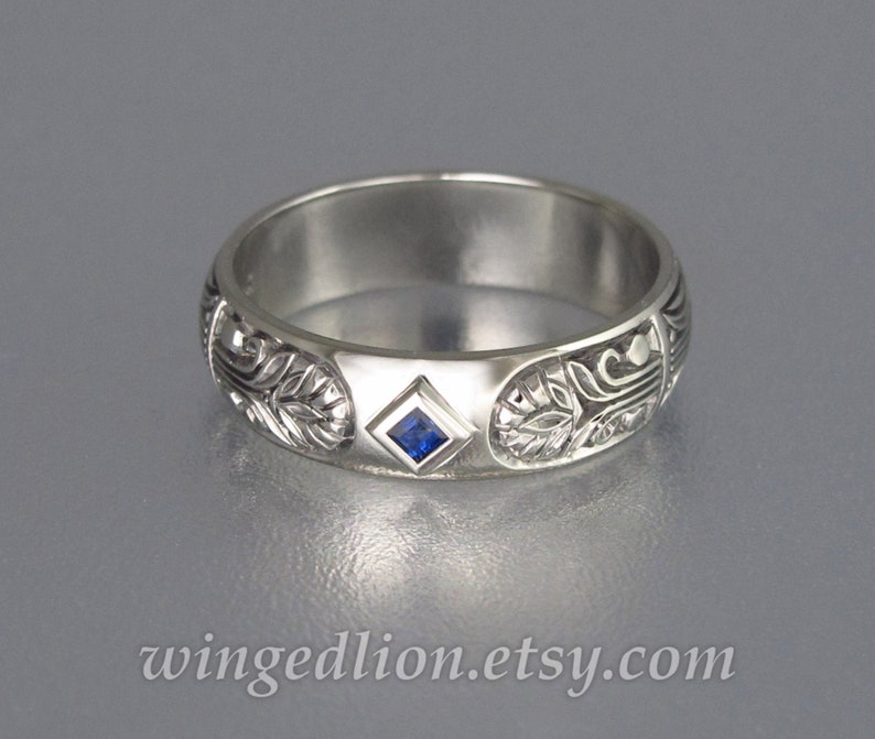 May include: A silver band with an intricate floral design and a small, square, blue sapphire gemstone.