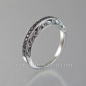 Op de afbeelding: Een zilveren bandring met een delicaat bloemmotief en zwarte edelstenen. De ring is bezet met kleine zwarte diamanten.