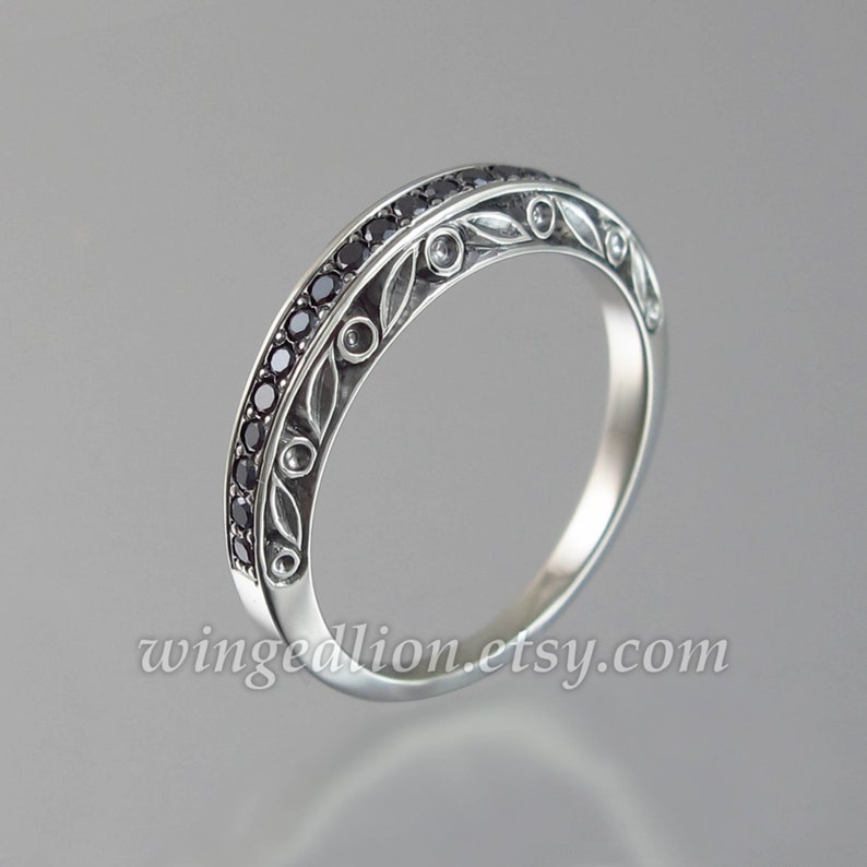 Op de afbeelding: Een zilveren bandring met een delicaat bloemmotief en zwarte edelstenen. De ring is bezet met kleine zwarte diamanten.