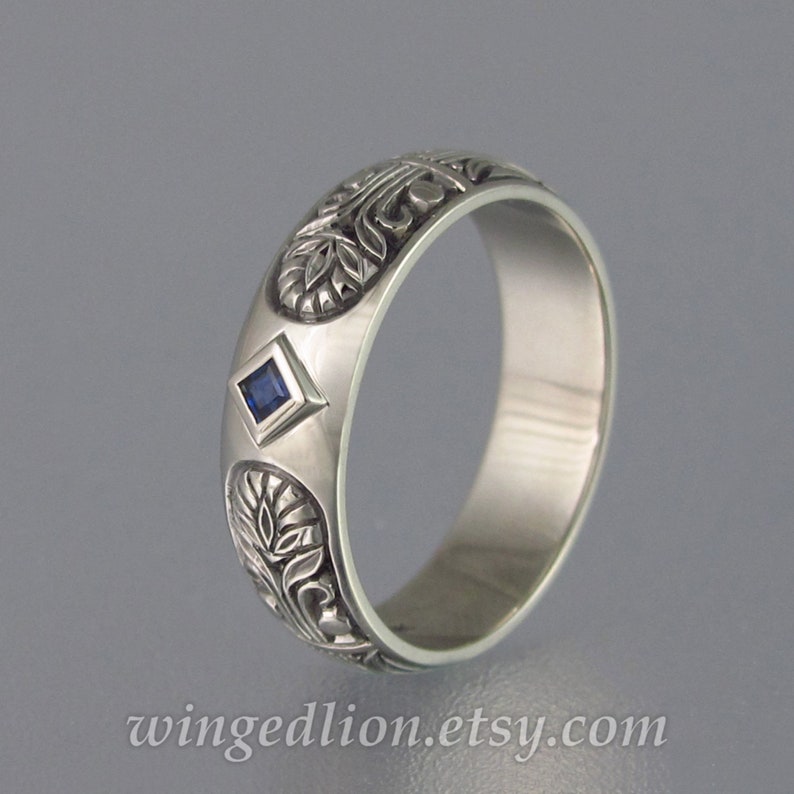 May include: A silver band ring with an intricate floral design and a small, square, blue sapphire gemstone.