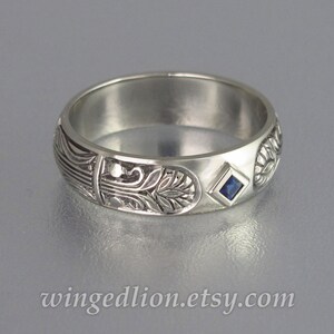 May include: A silver band ring with an intricate floral design and a small, square, blue sapphire gemstone.
