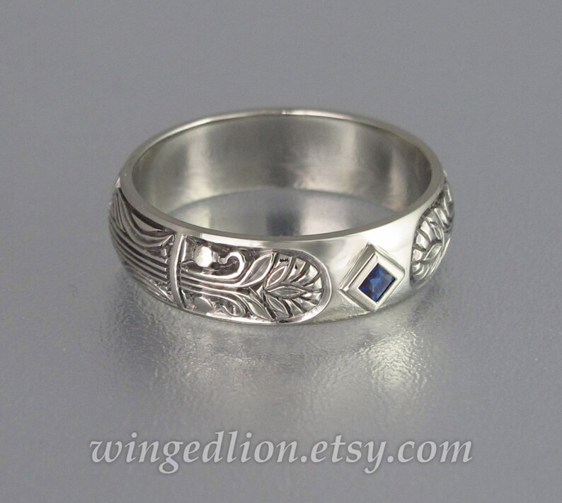 May include: A silver band ring with an intricate floral design and a small, square, blue sapphire gemstone.