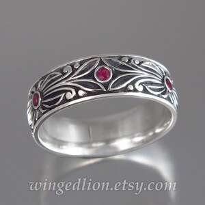 May include: A silver band ring with an intricate floral design and three red gemstones. The ring is polished and has a smooth finish.