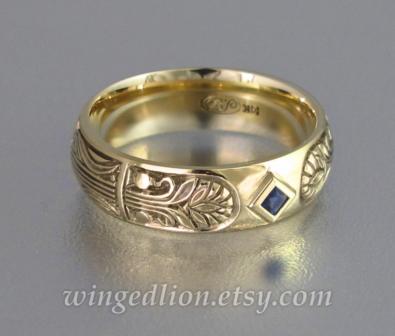 May include: A gold band with an intricate floral design and a small blue sapphire gemstone. The band is engraved with the initials "R" and "K".