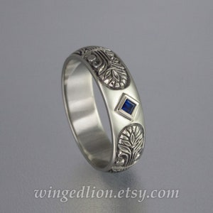 May include: A silver band ring with an intricate floral design and a small blue sapphire gemstone.