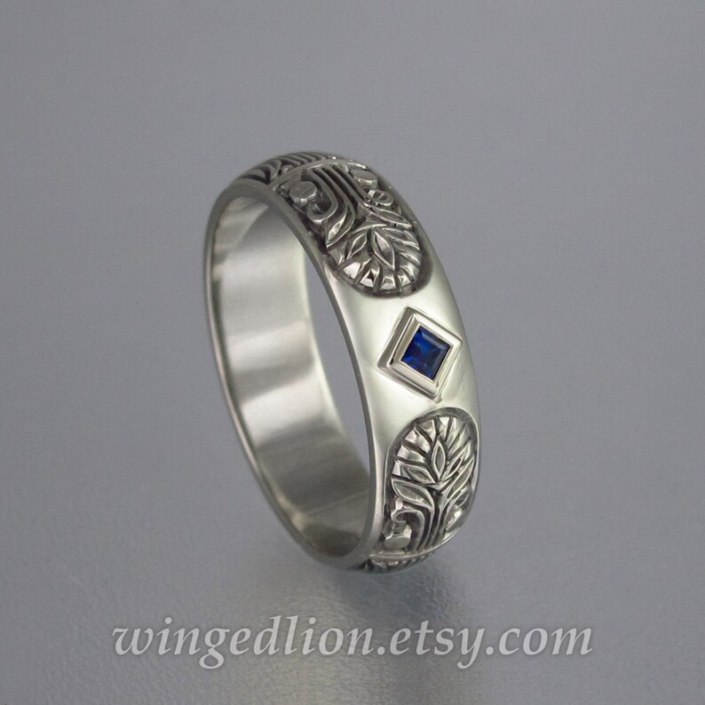 May include: A silver band ring with an intricate floral design and a small blue sapphire gemstone.
