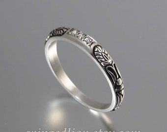 May include: A silver band ring with a delicate floral design and small clear stones.