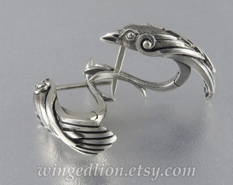 May include: A pair of silver earrings featuring a stylized bird design. The earrings are made of metal and have a textured finish.
