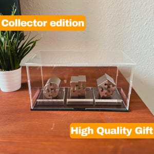 May include: Three metal puzzle pieces in a clear display case on a wooden surface. The case has a black base and the text "Collector edition" is visible above the case. The text "High Quality Gift" is visible below the case.