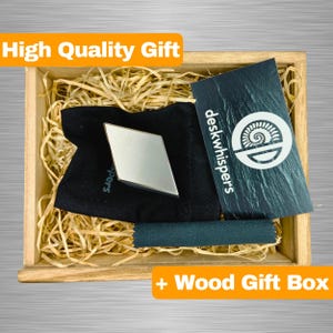 May include: A wooden gift box containing a black velvet pouch with a silver diamond-shaped paperweight. The box also includes a black card with the text "deskwhispers" and a logo.