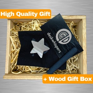 May include: A wooden gift box filled with wood shavings contains a black pouch with a silver star-shaped fidget toy, a black and silver business card with the text "deskwhispers", and a black stick. The box has a label that reads "High Quality Gift + Wood Gift Box".