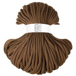 Può includere: Un gomitolo di cordoncino per macramè marrone. Il cordoncino è avvolto con una fascia bianca con la scritta "outlet" stampata sopra. Il cordoncino è di un colore marrone ricco e uniforme, e la consistenza appare morbida e flessibile.