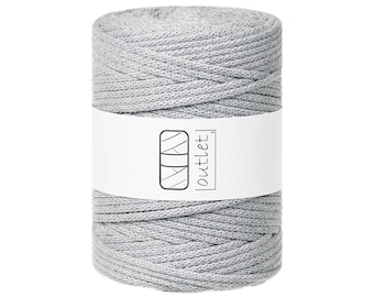 Puede incluir: Un carrete de cordón de macramé gris claro. Una etiqueta blanca envuelve el centro del carrete, mostrando un logotipo y la palabra "outlet". El cordón está bien enrollado, mostrando una superficie texturizada.