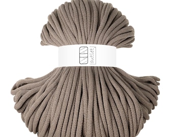 May include: A bundle of taupe-colored macrame cord. The cord is tightly wound and wrapped with a white label that reads "outlet" in a stylized font. The cord is suitable for various crafting projects.