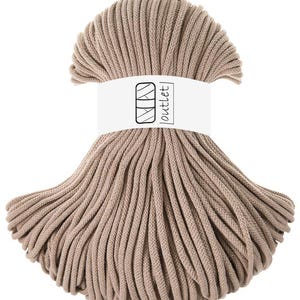 Può includere: Una matassa di corda marrone chiaro avvolta in una fascia di carta bianca con un'icona nera di un rocchetto di filo e il testo outlet. La corda è composta da molteplici fili di materiale intrecciato, disposti a ventaglio con una fascia centrale.