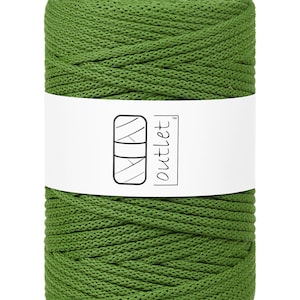 Op de afbeelding: Een cilindrische spoel groen macramé koord. Een wit label met het woord "outlet" en een logo omwikkelt het midden. Het koord is strak gewikkeld en heeft een getextureerd oppervlak. Ideaal voor knutsel- en doe-het-zelfprojecten.