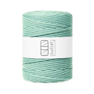 Puede incluir: Un carrete de cordón de macramé verde claro. El cordón está enrollado sobre sí mismo en forma cilíndrica. Una etiqueta blanca con el texto "MAY outlet" está envuelta alrededor del centro del carrete.